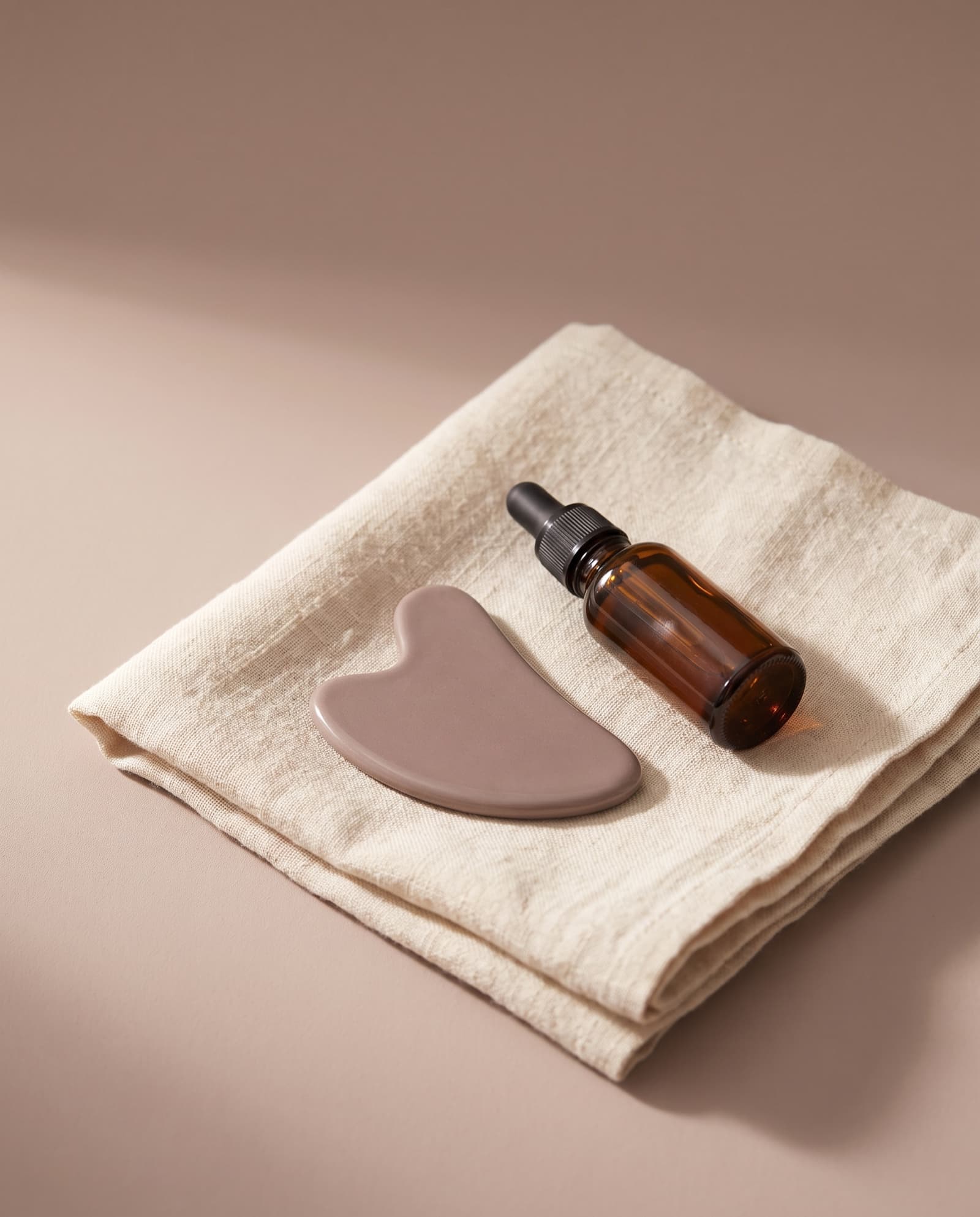 Gua sha sten og serum på foldet linned i studiets rolige toner